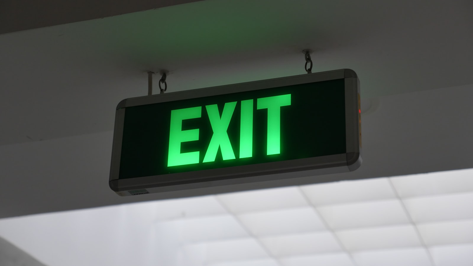 Illuminated green emergency exit sign suspended from a ceiling